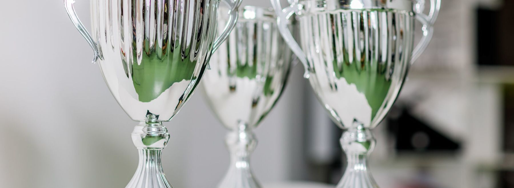 Drei glänzende silberne Trophäen stehen nebeneinander auf einem Tisch.