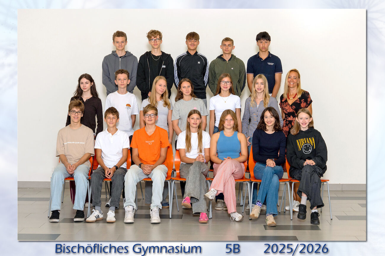 Klassenfoto mit sitzenden und stehenden Schülern und einem Lehrer in drei Reihen in einem Raum.