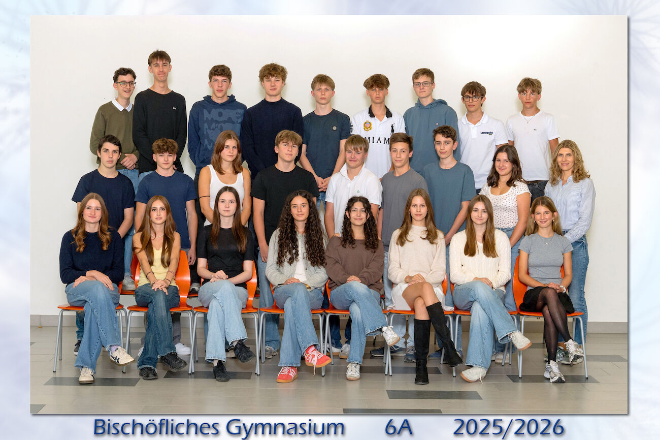 Eine Schulklasse und ihr Lehrer posieren für ein Gruppenfoto in einer Halle.