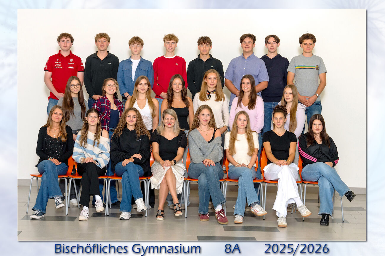 Ein Klassenfoto mit 25 Schülern und einer Lehrerin, die in einer Halle des Bischöflichen Gymnasiums posieren.