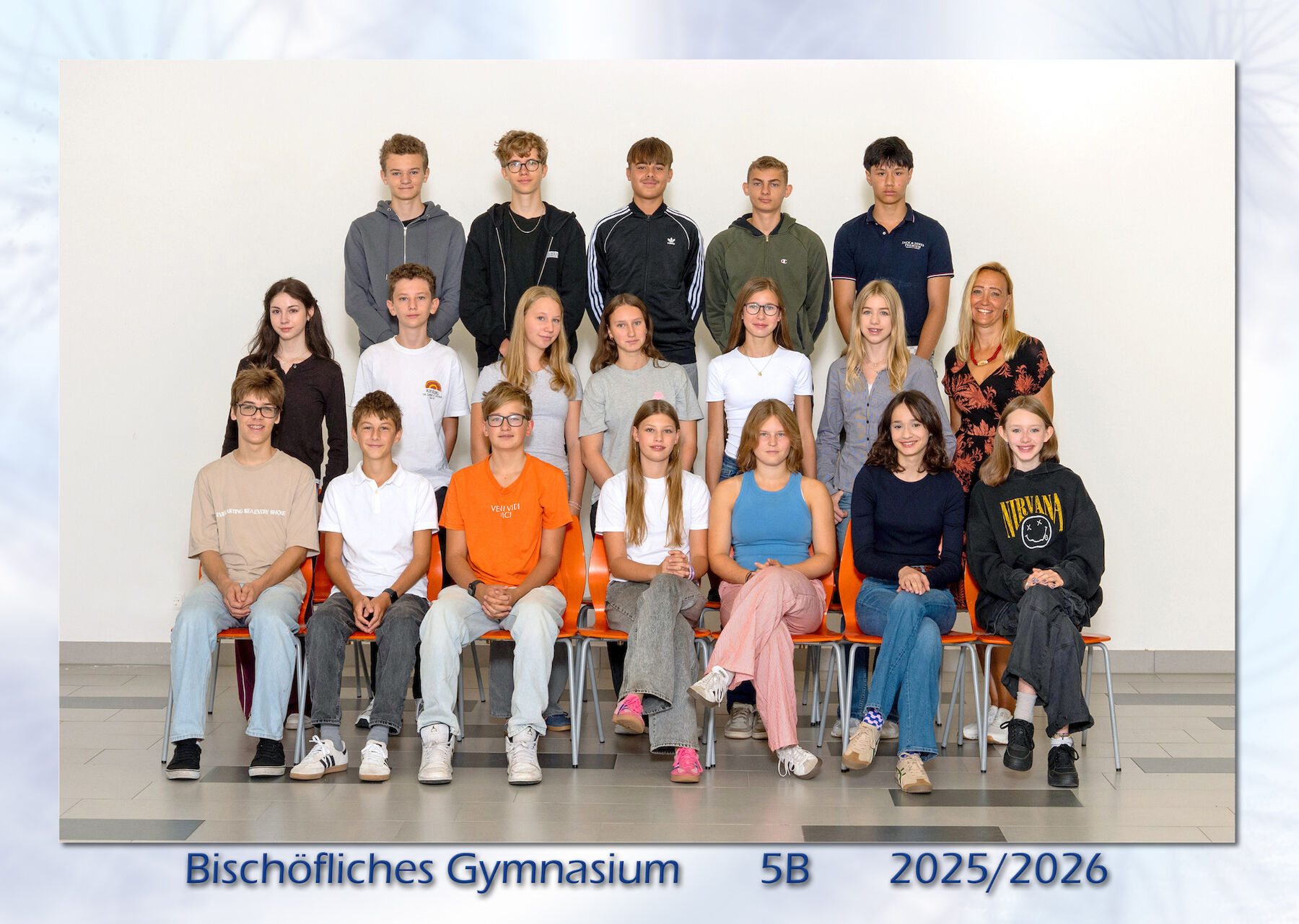 Eine Gruppe von Schülern und ein Lehrer posieren für ein Klassenfoto auf Stühlen und im Stehen.