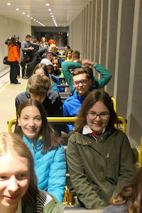 Eine Gruppe lächelnder Menschen, die in Reihen auf einem Fahrgeschäft im Vergnügungspark sitzen.