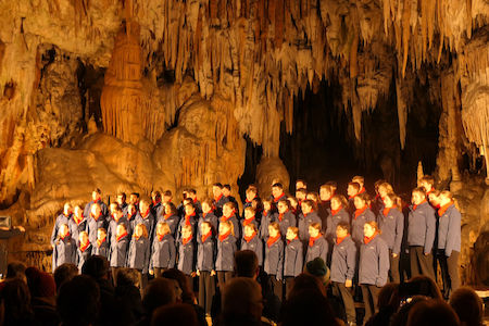 Ein Chor singt in einer von Stalaktiten und Stalagmiten umgebenen Höhle.