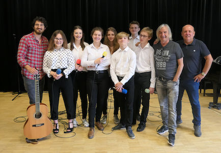 Eine Gruppe von Menschen posiert in einem Raum mit Mikrofonen und einer Gitarre.