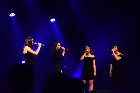 Vier Frauen singen auf der Bühne unter blauen Scheinwerfern.