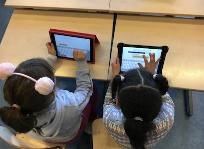 Zwei junge Mädchen benutzen Tablets, während sie in einem Klassenzimmer sitzen.