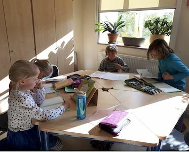 Vier kleine Kinder sitzen an einem Tisch in einem sonnendurchfluteten Klassenzimmer und lesen und schreiben.