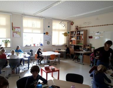 Kinder und ein Lehrer arbeiten in einem hellen, modernen Klassenzimmer mit Tischen und Stühlen.