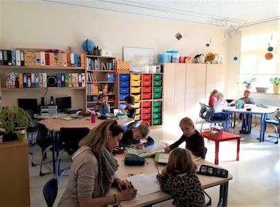 Ein Lehrer hilft jungen Schülern bei der Arbeit an den Tischen in einem hellen, gut organisierten Klassenzimmer.