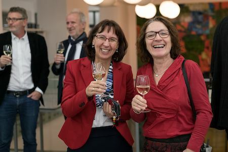 Zwei Frauen lächeln und halten Weingläser bei einem geselligen Beisammensein.