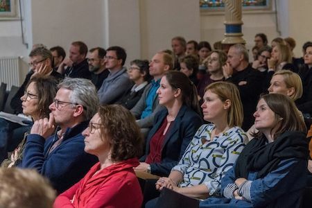 Aufmerksame Zuhörer bei einer Veranstaltung oder einem Seminar in einer Halle, in Reihen sitzend.