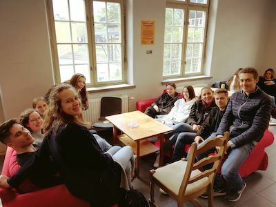 Eine Gruppe junger Leute sitzt in einem gemütlichen Raum um einen Holztisch herum.