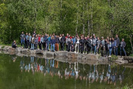 Eine große Gruppe von Menschen steht auf Felsen an einem Teich mit Bäumen im Hintergrund.