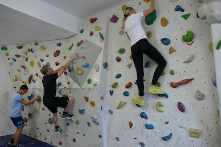 Drei Personen beim Indoor-Klettern an einer weißen Wand mit bunten Griffen.