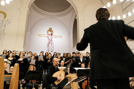 Ein Dirigent leitet einen Chor und Musiker während einer Aufführung in einer Kirche.