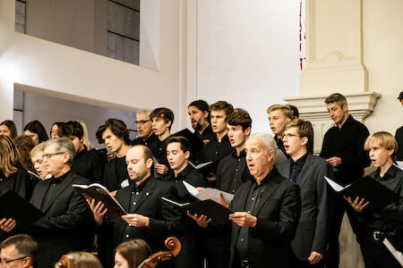 Ein Chor von Männern in schwarzer Kleidung singt gemeinsam in einer Kirche.