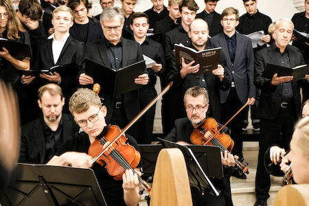 Ein Chor singt hinter Geigern, die bei einer offiziellen Musikaufführung spielen.