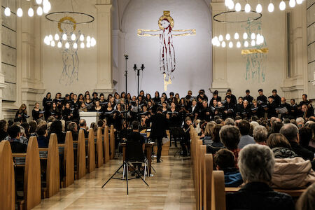 Chor, der in einer Kirche auftritt, mit einem Publikum, das in Holzbänken sitzt.