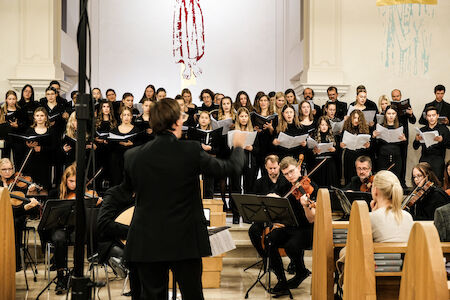 Ein Chor und ein Orchester treten gemeinsam in einer Kirche auf und werden von einem Dirigenten geleitet.