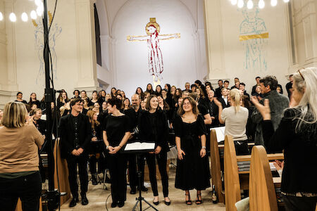 Ein schwarz gekleideter Chor steht nach einem Auftritt in einer Kirche und lächelt.