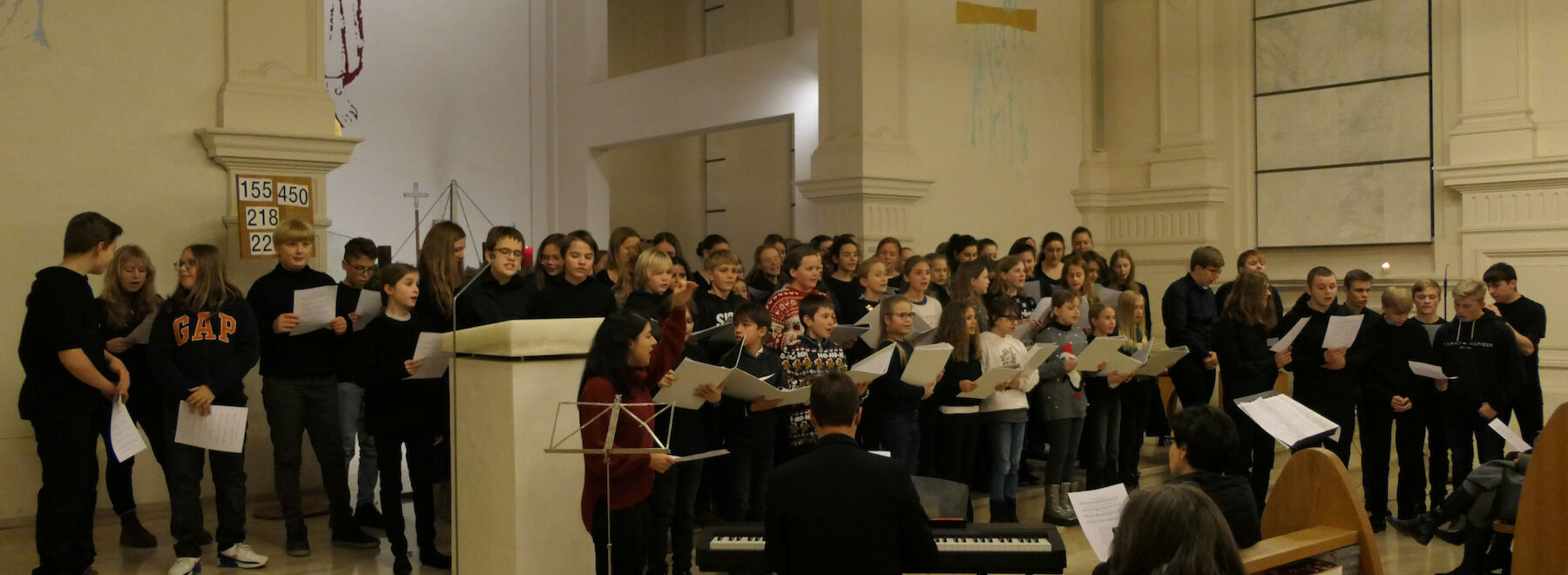 Ein großer Chor singt in einer Kirche, vor ihm stehen ein Pianist und ein Dirigent.
