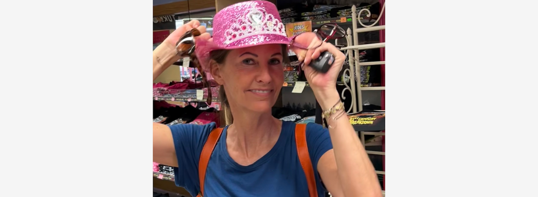 Eine lächelnde Frau mit Sonnenbrille auf dem Kopf steht vor einer großen Grünpflanze.