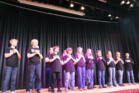 Zehn Kinder in schwarzen Hemden stehen auf der Bühne und legen ihre Hände auf die Brust.