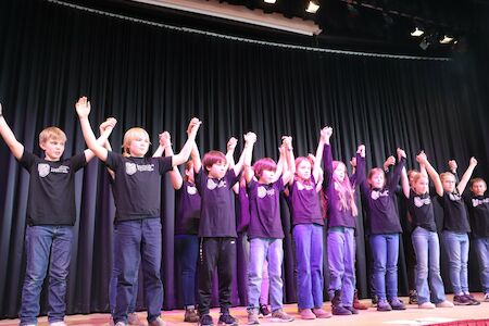 Kinder in schwarzen Hemden stehen auf der Bühne und halten sich mit erhobenen Armen an den Händen.