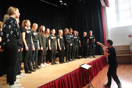 Ein Chor von Teenagern tritt auf der Bühne auf, während ein Dirigent sie leitet.