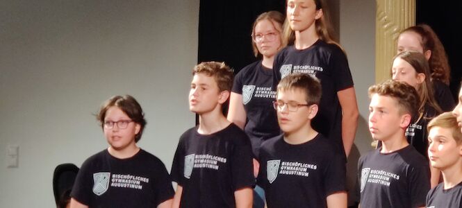 Eine Gruppe von Kindern singt auf der Bühne und trägt passende schwarze T-Shirts.