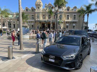Ein schwarzer Audi, geparkt vor einem prächtigen, verschnörkelten Gebäude mit Menschen in der Nähe.