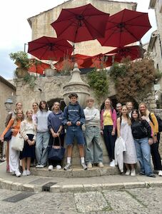 Eine Gruppe von Menschen posiert an einem Steinbrunnen mit roten Regenschirmen über ihnen.