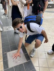 Ein lächelnder Junge mit Sonnenbrille steckt seine Hand in eine Sterntafel auf dem Bürgersteig.
