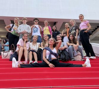 Eine Gruppe von Teenagern posiert lächelnd auf einer roten Treppe, einer macht vorne einen Spagat.