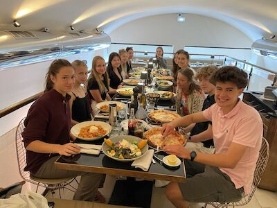 Eine Gruppe Jugendlicher sitzt an einem langen Tisch in einem Restaurant und genießt eine gemeinsame Mahlzeit.