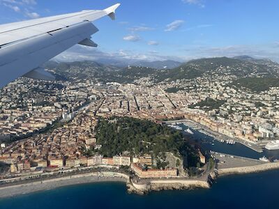 Blick aus dem Flugzeugfenster über eine Stadt an der Küste mit Bergen im Hintergrund.