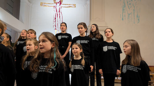 Ein Mädchenchor singt in einer Kirche und trägt passende schwarze Hemden.
