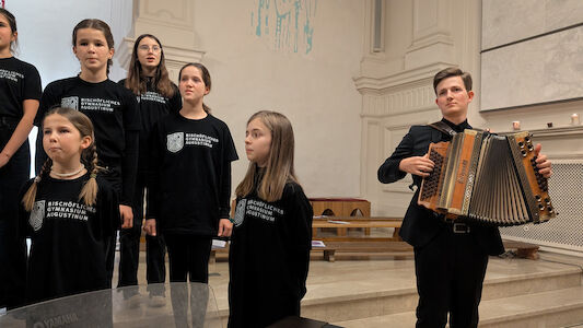 Eine Gruppe von Mädchen singt, während ein Junge in einer Kirche Akkordeon spielt.