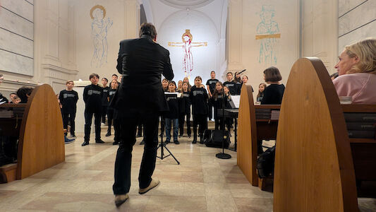 Ein Chor tritt in einer Kirche auf, während ein Dirigent ihn vom Kirchenschiff aus leitet.