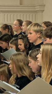 Eine Gruppe von Kindern, die in einem Chor singen und Notenblätter in der Hand halten.