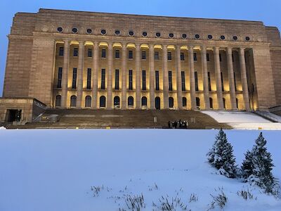 Ein großes, beleuchtetes Gebäude mit Säulen, verschneiten Stufen und kleinen Kiefern.