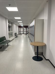 Ein leerer Flur mit Spinden, Bänken und einem runden Tisch an einer weißen Wand.