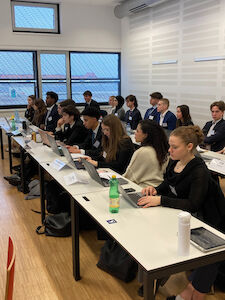 Studenten in Business-Kleidung sitzen an Tischen mit Laptops in einem Klassenzimmer.