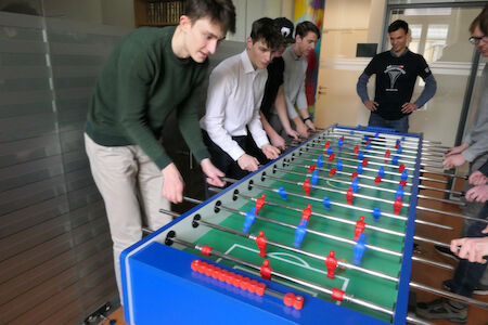 Sechs Personen spielen zusammen in einem Büro eine Partie Tischfußball.