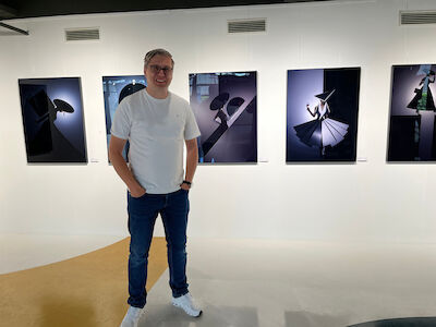Eine Person in weißem Hemd und Jeans steht vor einem gerahmten Kunstwerk in einer Galerie.