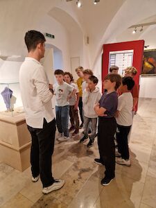 Eine Gruppe von Kindern hört einem Mann zu, der in einer Kunstgalerie spricht.