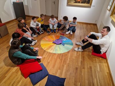 Eine Gruppe von Jungen sitzt im Kreis um ein buntes Rad auf einem Holzboden.
