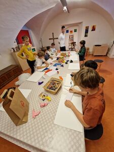 Kinder sitzen um einen Tisch herum und malen und basteln in einem Kunstunterrichtsraum.