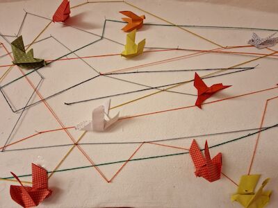 Origami-Vögel, die an bunten Schnüren auf weißem Hintergrund befestigt sind.