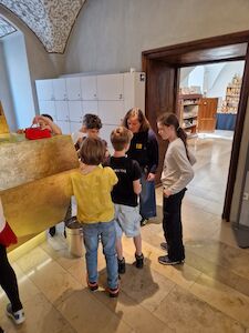 Fünf Kinder stehen in einem Museums- oder Galerieflur und unterhalten sich miteinander.